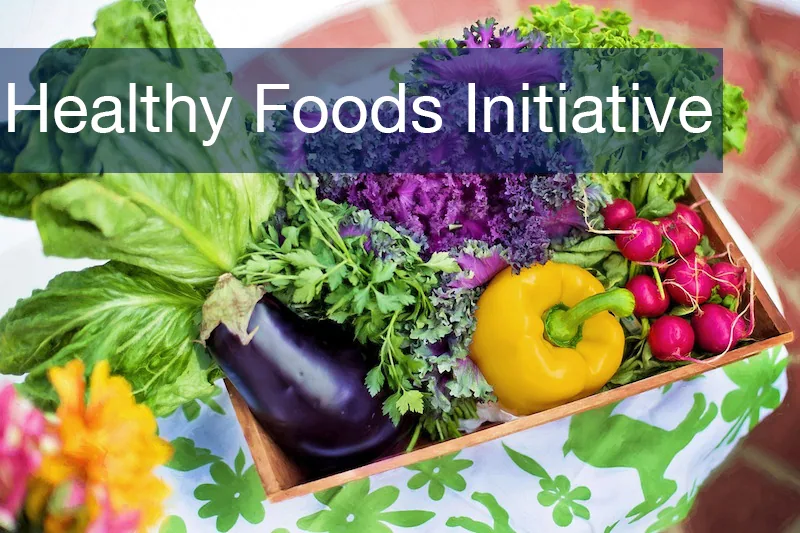 Wooden box filled with fresh vegetables including lettuce, purple kale, eggplant, yellow pepper, and radishes