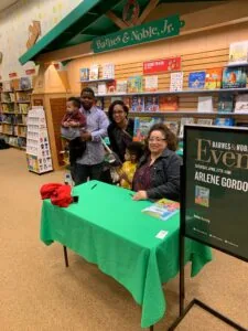 Author event at Barnes & Noble bookstore with woman seated at green table and family members standing nearby
