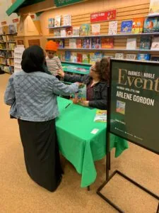 Woman and child at green table at book signing event in bookstore with shelves of books visible behind them