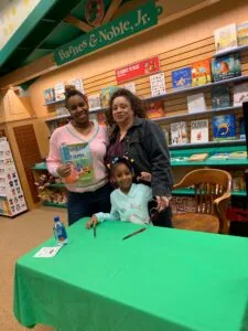 Two adults and a child at a green table in a Barnes & Noble bookstore, with bookshelves visible behind them