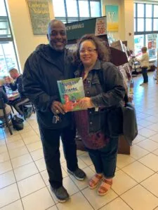 Two people holding a children's book titled "Bluebird Friends" inside a bookstore with displays and signage visible in the background.