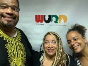 Three smiling people posing together in front of a colorful logo backdrop