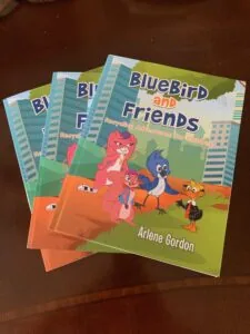 Three copies of children's book titled BlueBird and Friends featuring illustrated characters on cover with city buildings in background