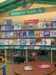 Barnes & Noble Jr. bookstore display with shelves of children's books, plush toys, and merchandise beneath a green storefront sign