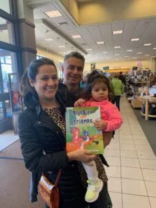 Two adults and a young child holding a children's book in a library setting