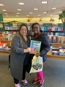 Two people holding a Blue Bird Friends book in a library with bookshelves behind them