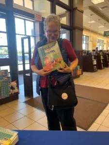 Person holding a children's book titled Bluebird Friends inside a library entrance area