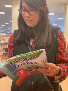 Person wearing glasses and red plaid shirt holding Bluebird Friends book in library
