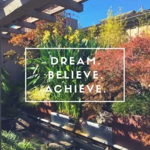 Garden with autumn foliage and green plants with white text overlay reading 'DREAM BELIEVE ACHIEVE'